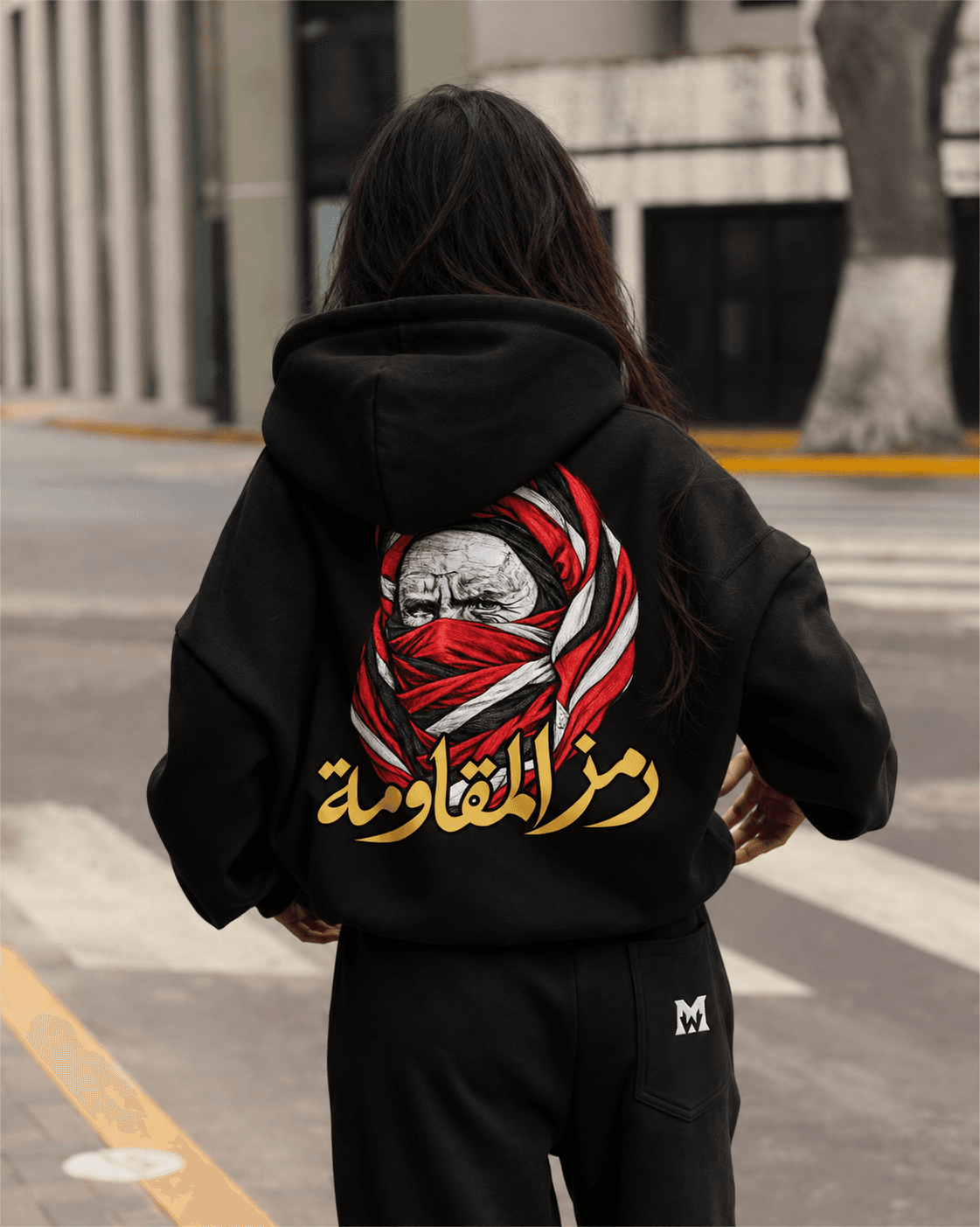 Femme de dos près d’un passage piéton, portant le hoodie noir au portrait rouge et blanc et à la calligraphie dorée.